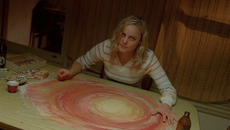 Candy encara a câmera diante de uma espiral pintada sobre a mesa