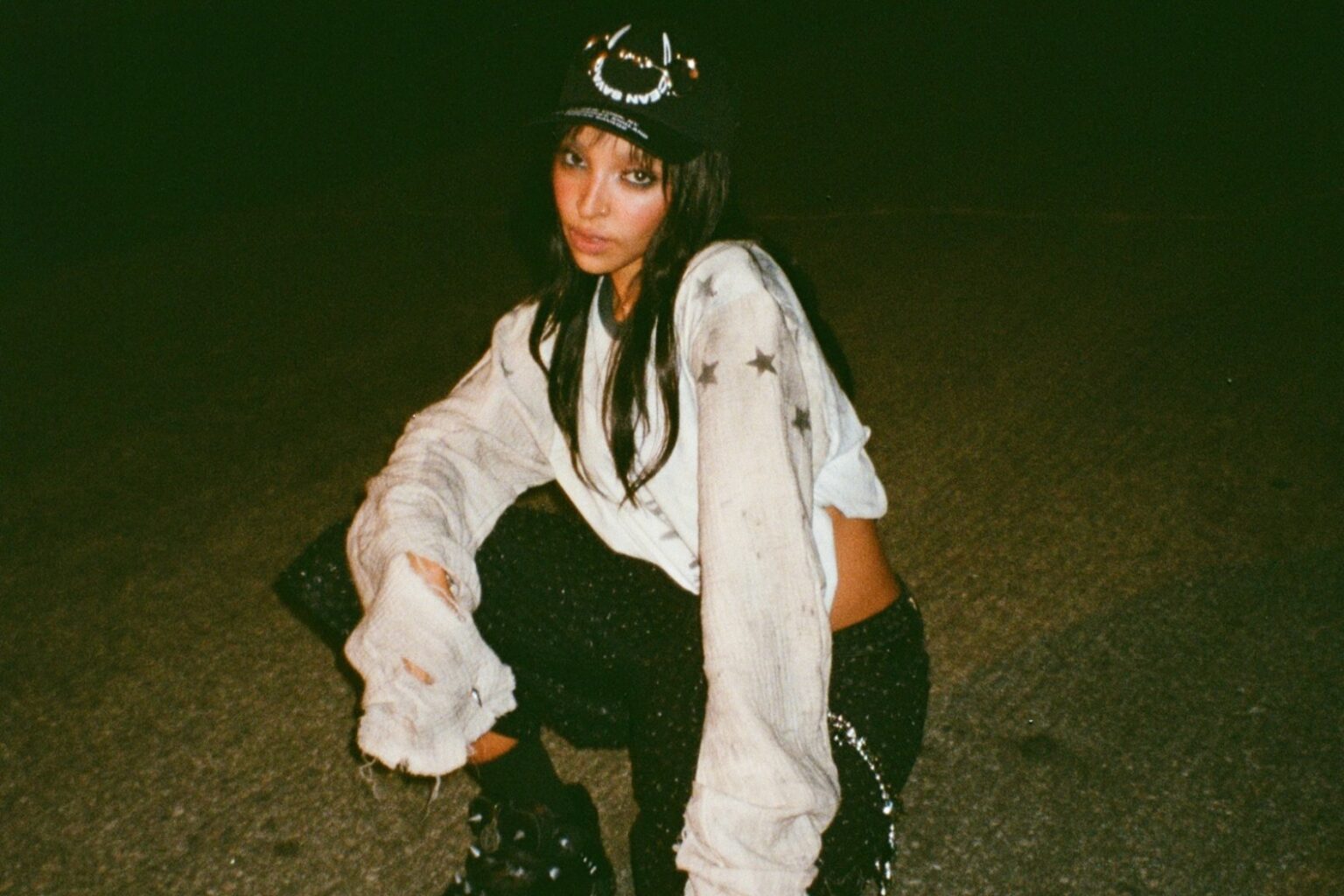 Tinashe agachada em uma cena noturna da divulgação de POPSTAR